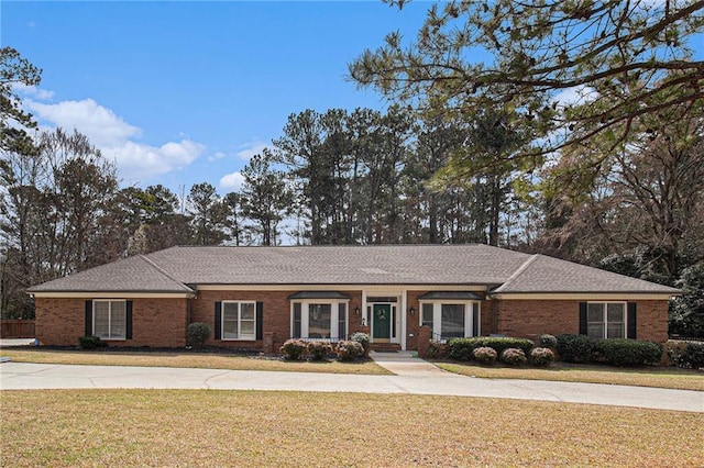 ranch-style house with a shingled roof, a front lawn, and brick siding