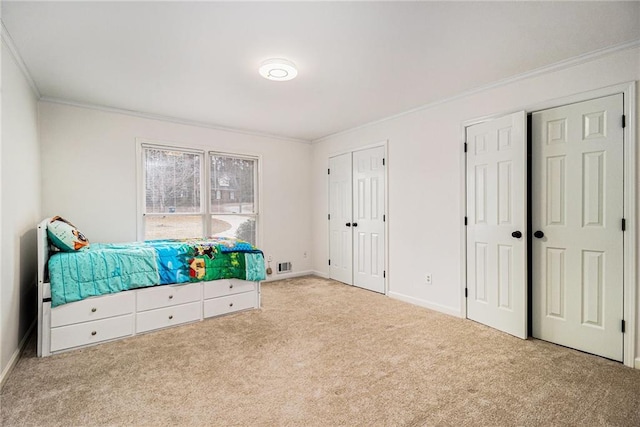 bedroom featuring baseboards, visible vents, crown molding, carpet floors, and multiple closets