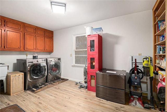 clothes washing area with wood finished floors, washing machine and clothes dryer, cabinet space, and baseboards