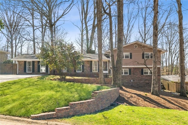 tri-level home featuring brick siding, a front lawn, and fence