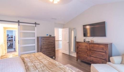 bedroom with lofted ceiling, a barn door, and dark hardwood / wood-style flooring