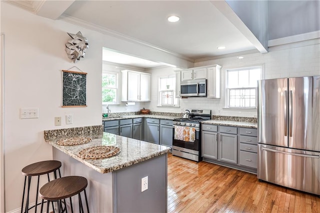 1136 Moreland Pl SE, Atlanta, GA 30316 - kitchen with appliances with stainless steel finishes, gray cabinetry, a kitchen breakfast bar, a peninsula, and light stone counters