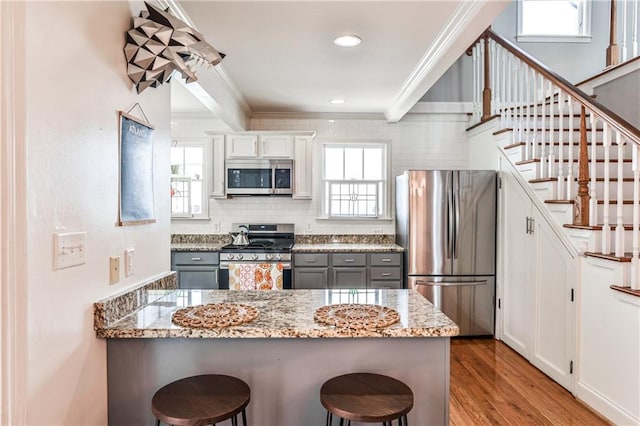 1136 Moreland Pl SE, Atlanta, GA 30316 - kitchen with stainless steel appliances, crown molding, a breakfast bar, wood finished floors, and a peninsula