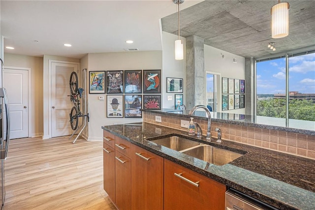 kitchen with sink, light hardwood / wood-style floors, dark stone countertops, and hanging light fixtures