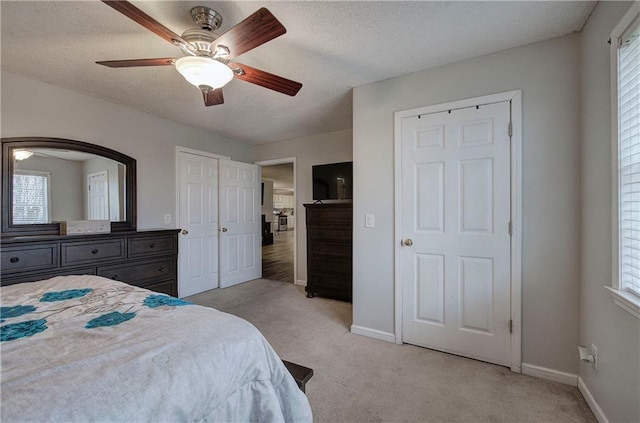 bedroom with light colored carpet, ceiling fan, a textured ceiling, and baseboards