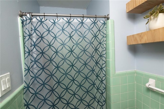 full bath with a shower with curtain, a wainscoted wall, and tile walls