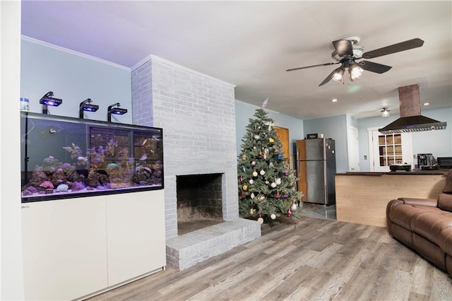 living area featuring ornamental molding, a brick fireplace, ceiling fan, and wood finished floors