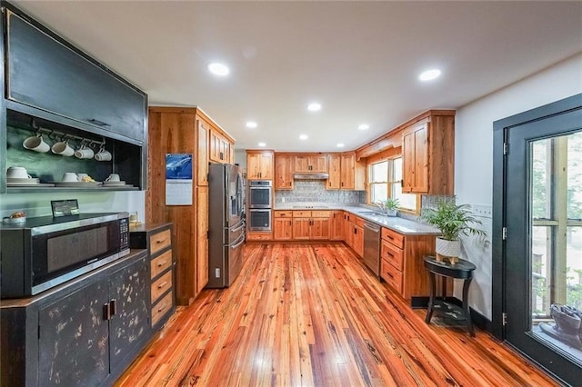 kitchen with a sink, appliances with stainless steel finishes, under cabinet range hood, recessed lighting, and light wood finished floors
