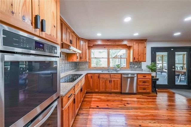 kitchen with tasteful backsplash, light wood-style floors, under cabinet range hood, appliances with stainless steel finishes, and a sink