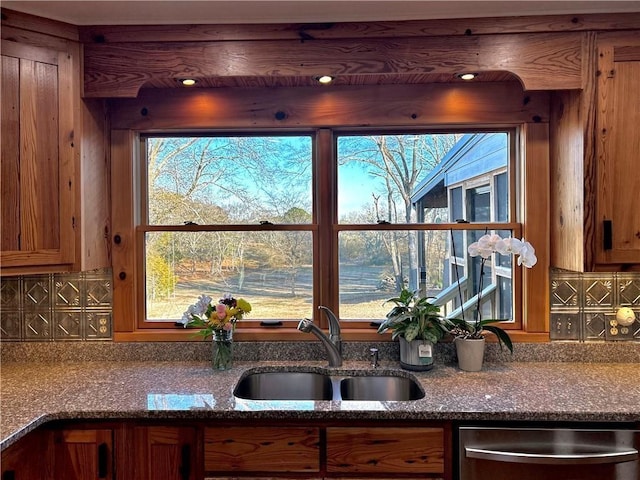 kitchen featuring dark stone countertops, brown cabinets, a sink, dishwasher, and backsplash