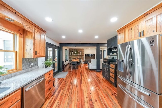 kitchen with recessed lighting, light stone counters, appliances with stainless steel finishes, backsplash, and light wood-type flooring
