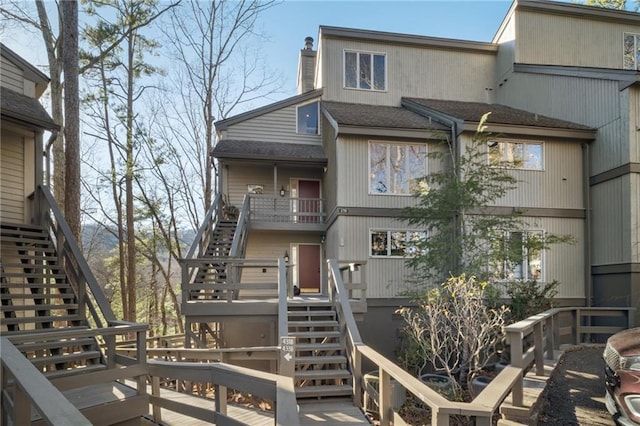 view of front facade featuring a wooden deck, stairway, roof with shingles, and a chimney