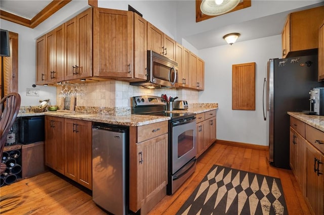 kitchen with light stone countertops, baseboards, light wood-style flooring, stainless steel appliances, and backsplash