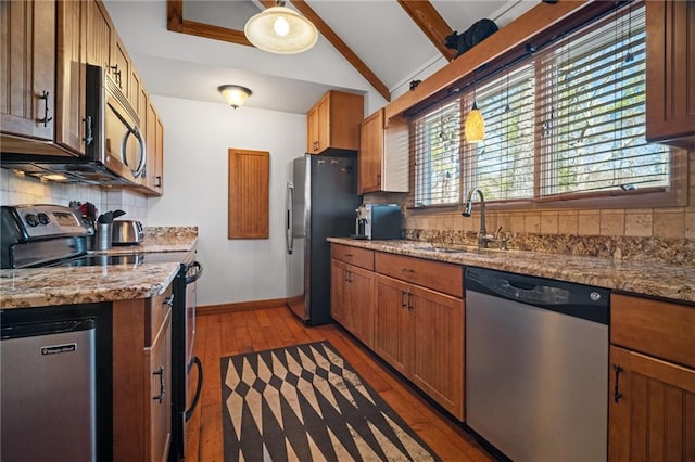 kitchen featuring vaulted ceiling with beams, a sink, stainless steel appliances, light wood-style floors, and tasteful backsplash