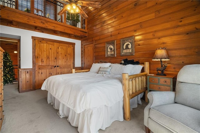 bedroom featuring light carpet, wooden walls, and a high ceiling