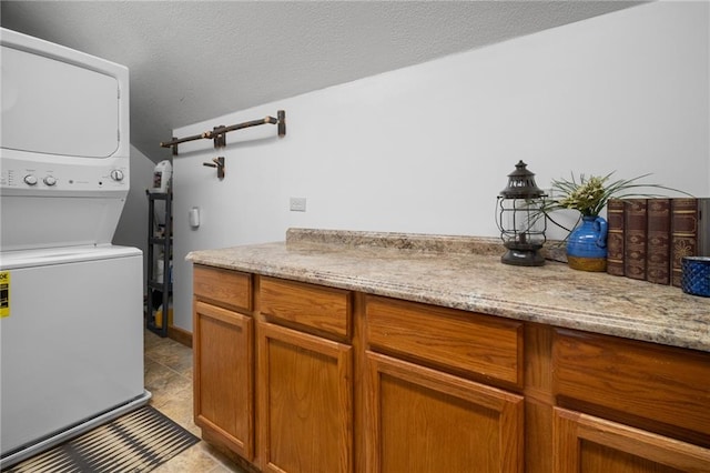 washroom with cabinet space, a textured ceiling, and stacked washing maching and dryer