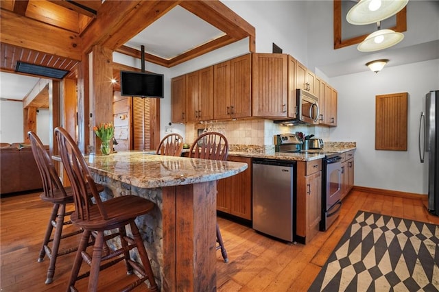 kitchen featuring baseboards, decorative backsplash, light wood-style flooring, appliances with stainless steel finishes, and a kitchen breakfast bar