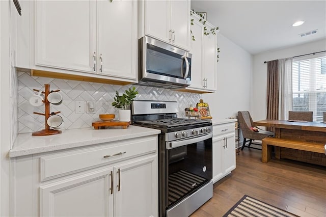 kitchen with appliances with stainless steel finishes, white cabinets, backsplash, light stone counters, and light hardwood / wood-style flooring