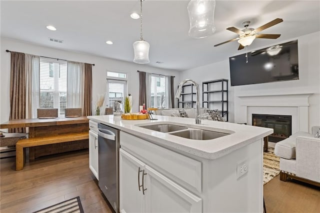 kitchen featuring decorative light fixtures, sink, white cabinets, stainless steel dishwasher, and a center island with sink