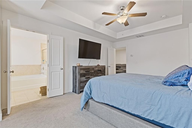 carpeted bedroom featuring a tray ceiling, ceiling fan, and ensuite bathroom