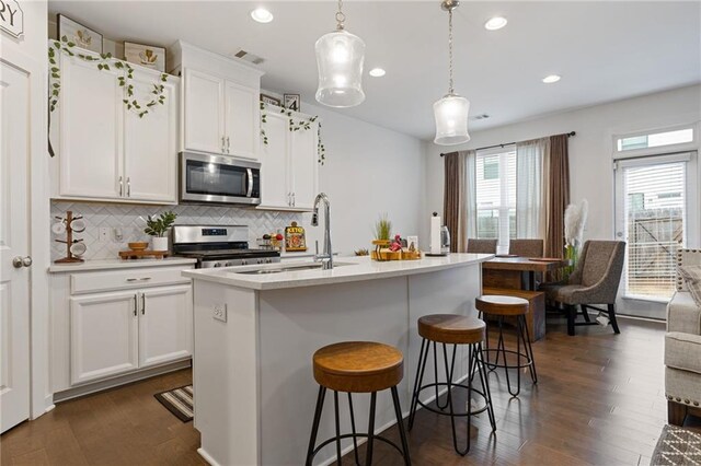 kitchen with decorative light fixtures, an island with sink, white cabinetry, backsplash, and stainless steel appliances