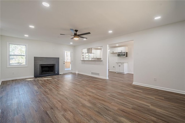 unfurnished living room with a brick fireplace, dark wood-style floors, visible vents, and a wealth of natural light