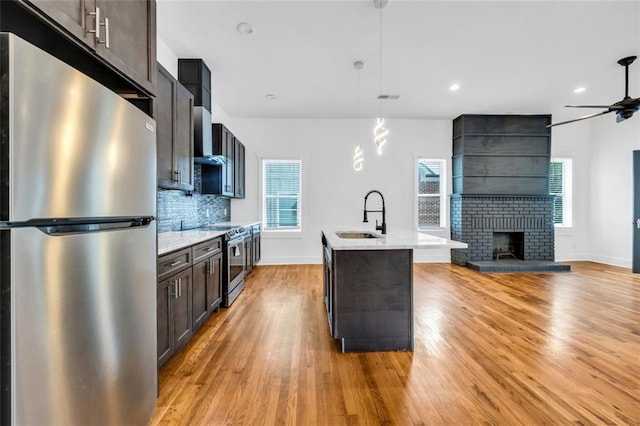 kitchen featuring pendant lighting, sink, a brick fireplace, a kitchen island with sink, and stainless steel appliances