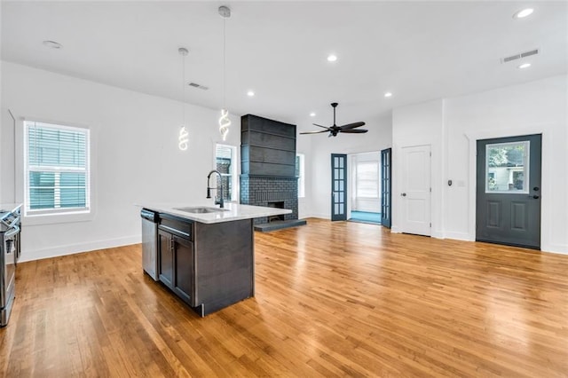 kitchen featuring light hardwood / wood-style floors, sink, a fireplace, a center island with sink, and decorative light fixtures