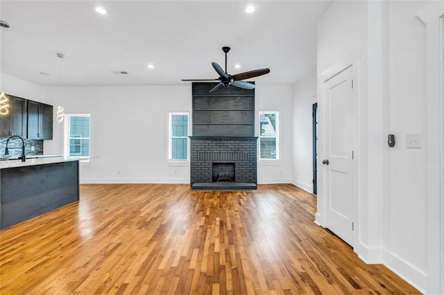 unfurnished living room featuring a brick fireplace, ceiling fan, plenty of natural light, and light wood-type flooring