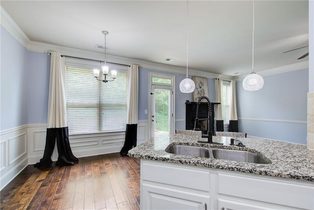 kitchen featuring a sink, light stone countertops, a wainscoted wall, crown molding, and white cabinets