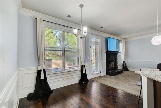 dining space with a chandelier, crown molding, dark wood-type flooring, a wainscoted wall, and a fireplace