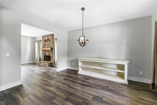 unfurnished living room featuring an inviting chandelier, a stone fireplace, and dark hardwood / wood-style flooring