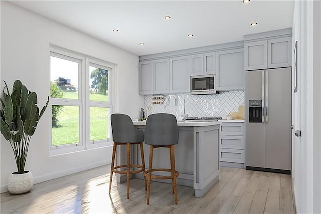 kitchen with stainless steel appliances, light wood-type flooring, gray cabinets, decorative backsplash, and a kitchen breakfast bar