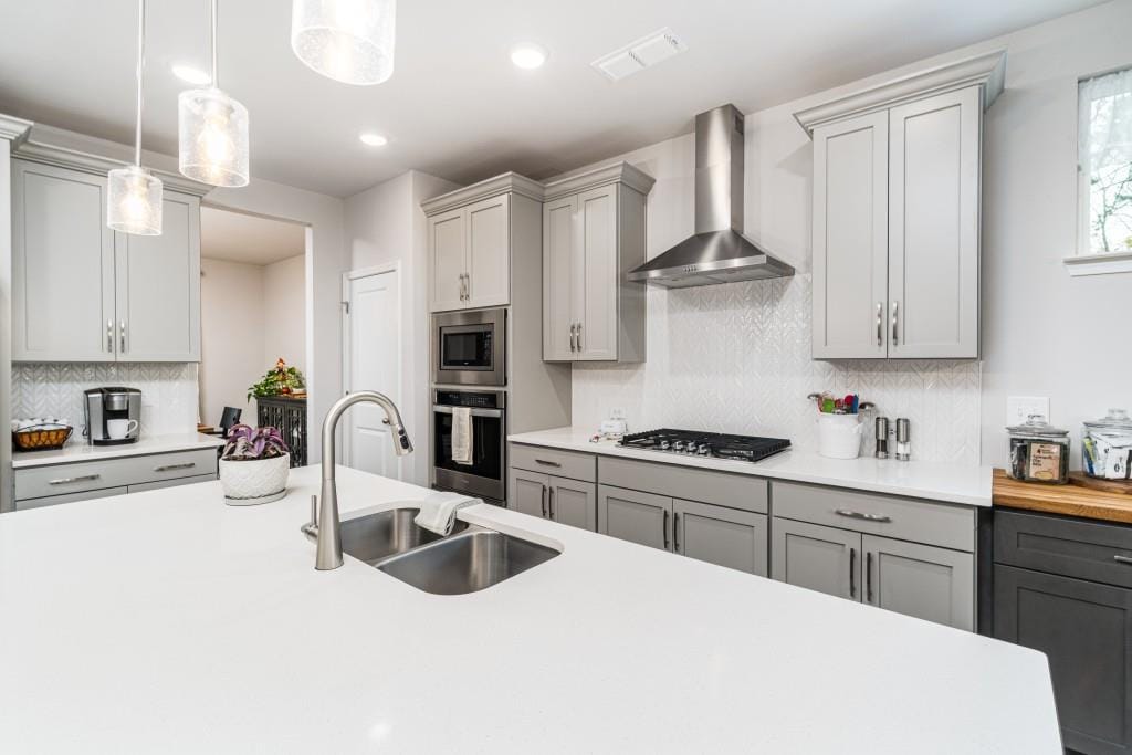 kitchen featuring sink, wall chimney exhaust hood, pendant lighting, gray cabinets, and appliances with stainless steel finishes