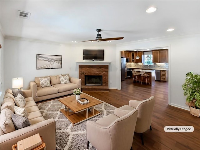 living area with dark wood-style floors, ornamental molding, a fireplace, and visible vents
