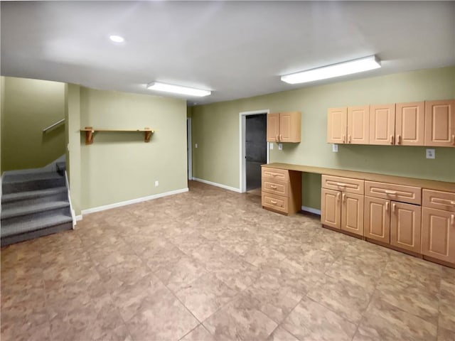 kitchen with light brown cabinetry, built in desk, light countertops, and baseboards