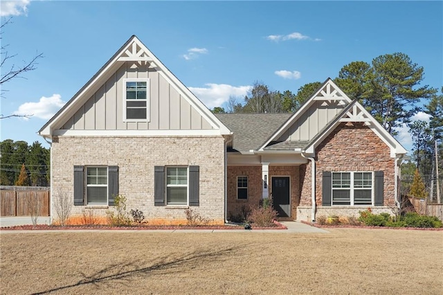 craftsman house with a shingled roof, brick siding, fence, board and batten siding, and a front yard