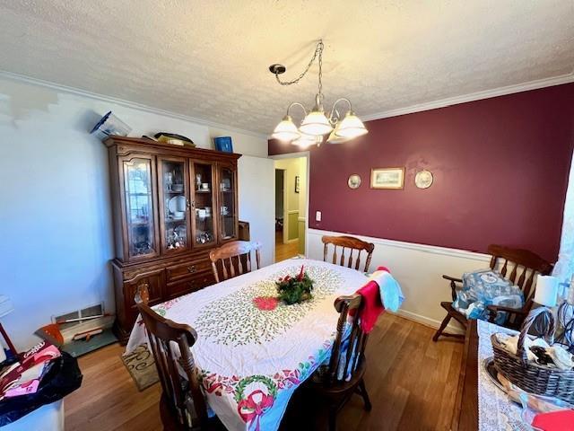 dining space featuring crown molding, a notable chandelier, wood finished floors, and a textured ceiling