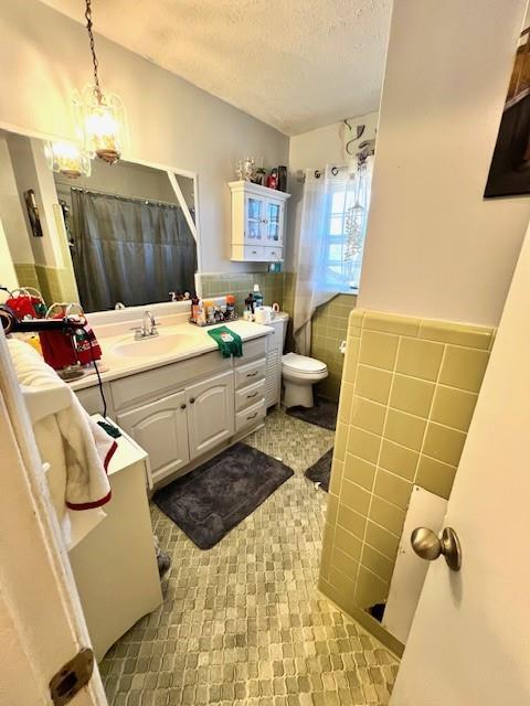 bathroom with vanity, a textured ceiling, wainscoting, tile walls, and toilet