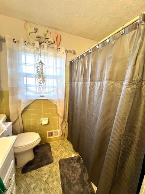 full bath featuring a shower with curtain, toilet, a textured ceiling, tile walls, and vanity