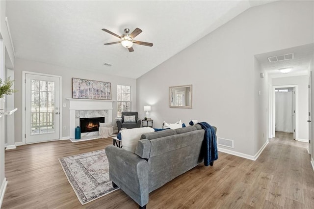 living room with ceiling fan, a premium fireplace, light hardwood / wood-style flooring, and lofted ceiling