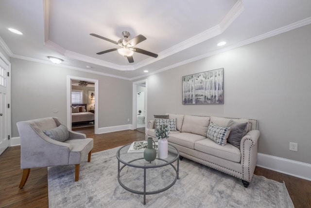 living room with a raised ceiling, crown molding, baseboards, and wood finished floors