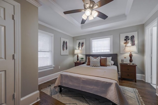 bedroom with ornamental molding, a tray ceiling, multiple windows, and wood finished floors