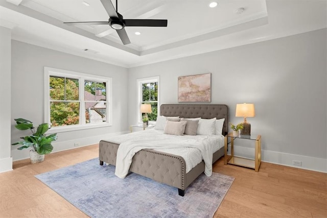 bedroom with ceiling fan, a raised ceiling, light hardwood / wood-style flooring, and crown molding