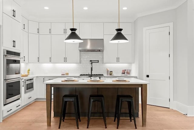 kitchen with a kitchen island with sink, light wood-type flooring, wall chimney exhaust hood, and white cabinets