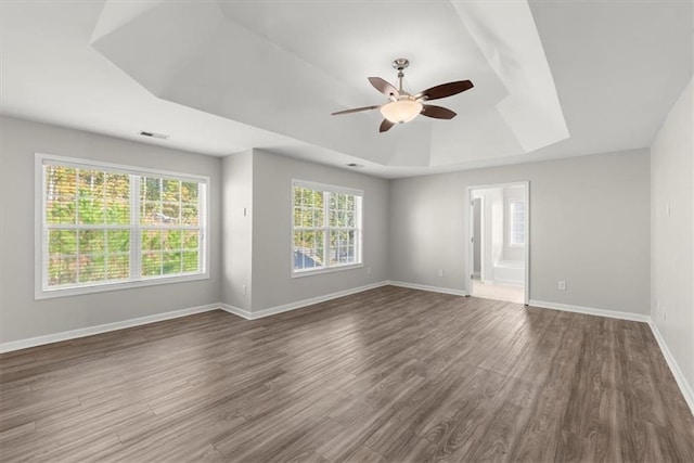 empty room featuring dark wood-type flooring, ceiling fan, and a tray ceiling