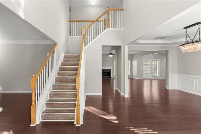 staircase with crown molding, hardwood / wood-style flooring, a high ceiling, and ceiling fan with notable chandelier