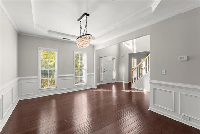 empty room featuring a notable chandelier, ornamental molding, a tray ceiling, and dark wood-type flooring