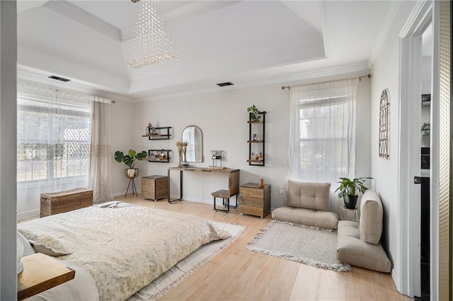 bedroom with light wood-style floors, visible vents, a tray ceiling, and ornamental molding