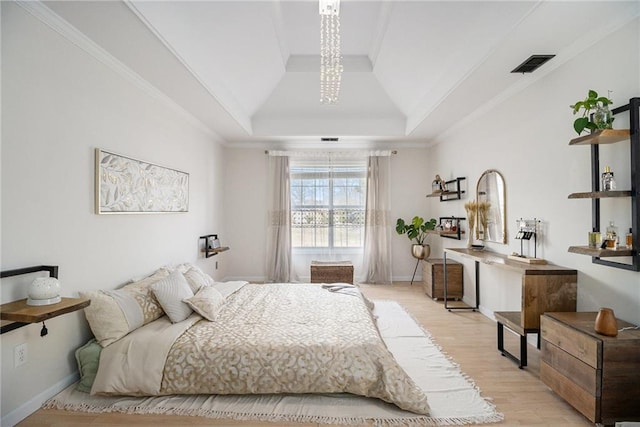 bedroom with baseboards, visible vents, light wood-style flooring, a tray ceiling, and crown molding